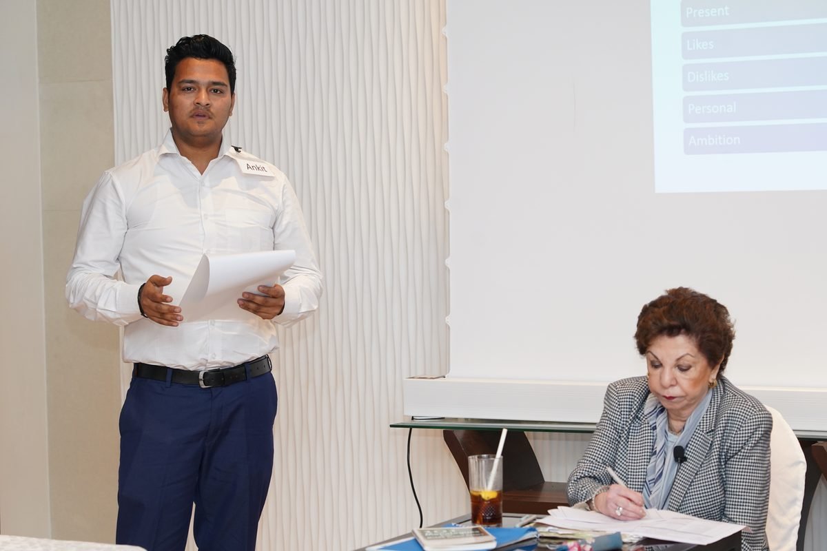 A participant introduces himself to the room while Sabira Merchant makes notes at her table
