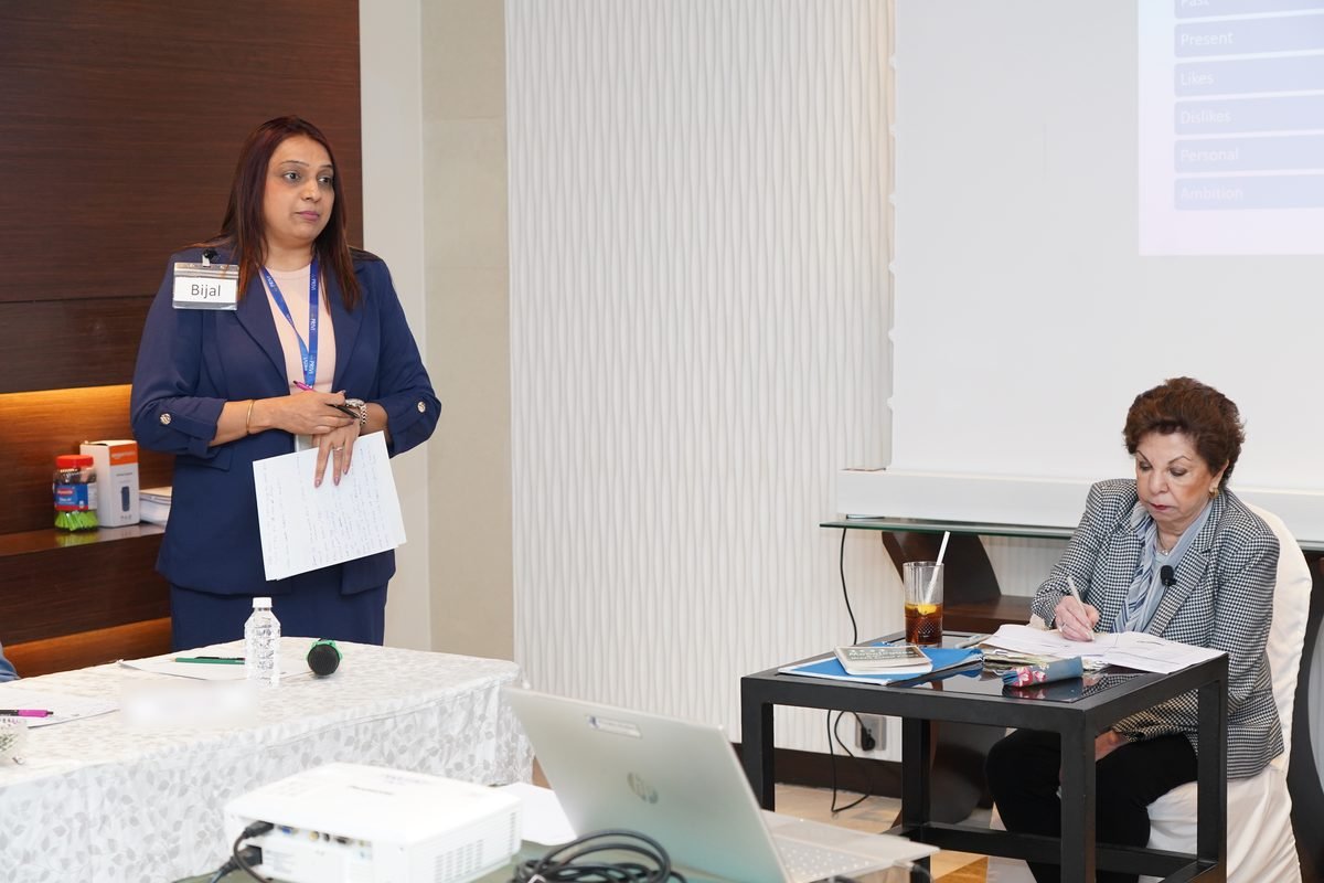 A participant speaks to the room while Sabira Merchant writes her assessment