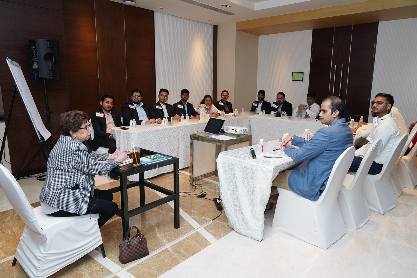 Sabira Merchant speaking with participants seated around a U-shaped table